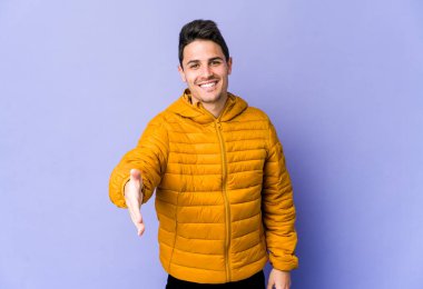 Mor arka planda izole edilmiş genç beyaz adam selamlama jesti olarak kameraya elini uzatıyor..