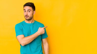 Sarı fırında izole edilmiş genç beyaz adam gülümsüyor ve boş alanda bir şeyler gösteriyor..