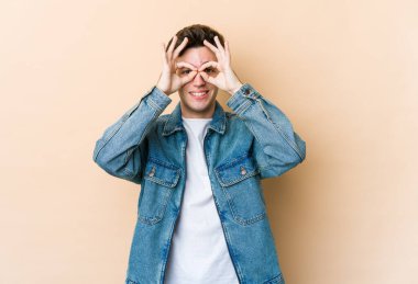 Beyazlı genç bir adam bej arka planda izole edilmiş, gözlerde sorun yok işareti var.