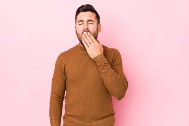 Pembe arka planda genç, beyaz bir adam izole edilmiş esniyor. Ağzı eliyle kapatan yorgun bir hareket sergiliyor..