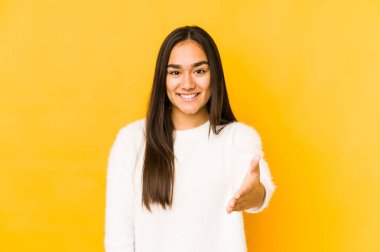 Sarı arka planda izole edilmiş genç bir kadın kameraya elini uzatarak selam veriyor..