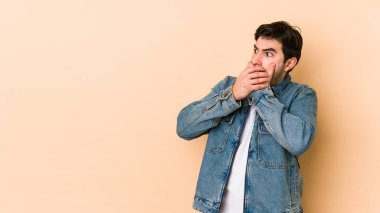 Genç adam bej arka planda izole edilmiş. Düşünceli bir şekilde bir fotokopi odasına bakıyor. Ağzını eliyle kapatıyor..