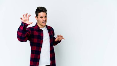 Beyaz arka planda izole edilmiş genç beyaz bir adam pençelerini kedi taklidi yaparken gösteriyor, agresif bir hareket..