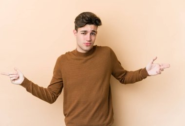 Beyazlı genç bir adam bej arka planda izole edilmiş sorgulama sırasında omuz silkiyor ve şüphe duyuyor..