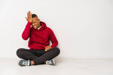 Yerde tek başına oturan genç Latin bir adam bir şeyi unutuyor. Alnına avuç içi ve gözlerini kapatarak vuruyor..