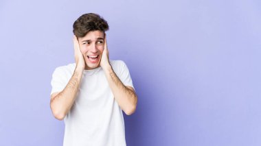 Kafkasyalı genç adam mor arka planda izole edilmiş kulakları kulaklarıyla kapatıyor çok fazla ses duymamaya çalışıyor..