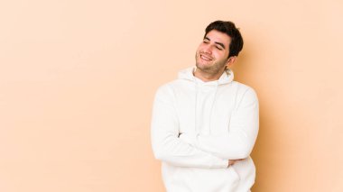 Bej arka planda izole edilmiş genç adam kollarını kavuşturarak gülümsüyor..
