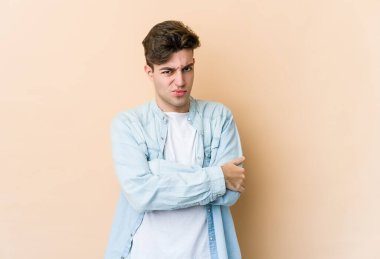 Beyazlı genç bir adam bej arka planda izole edilmiş hoşnutsuzca kaşlarını çatmış, kollarını kavuşturmuş..