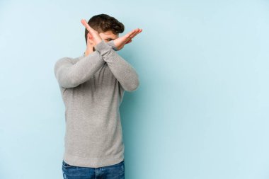 Kafkasyalı genç adam mavi arka planda izole edilmiş iki kolu çapraz tutuyor, inkar kavramı.