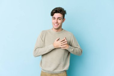 Mavi arka planda izole edilmiş beyaz bir genç, dost bir ifadeye sahip, avuçlarını göğsüne bastırıyor. Aşk konsepti.