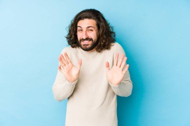 Uzun saçlı genç adam mavi bir arka planda izole edilmiş, tiksinti gösteren birini reddediyor..