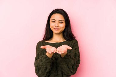 Pembe arka planda izole edilmiş genç Çinli bir kadın elinde avuç içi bir şeyle kameraya sunuyor..