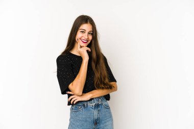 Beyaz arka planda izole edilmiş genç beyaz kadın mutlu ve kendinden emin gülümsüyor, elleriyle çenesine dokunuyor..