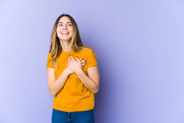 Mor arka planda soyutlanmış beyaz bir kadın. Gülüyor, elini kalbe koyuyor, mutluluk kavramını koruyor..