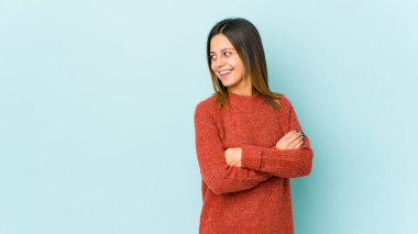 Mavi arka planda soyutlanmış genç bir kadın kollarını kavuşturarak gülümsüyor..