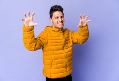 Mor arka planda izole edilmiş genç beyaz adam gergin ellerle çığlık atıyor..