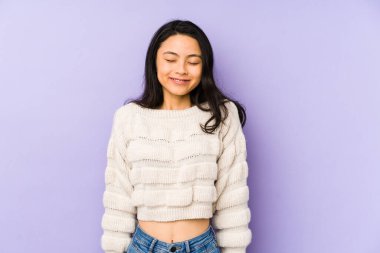 Mor bir arka planda izole edilmiş genç Çinli kadın gülüyor ve gözlerini kapıyor, rahatlamış ve mutlu hissediyor..