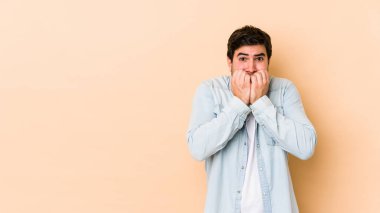 Bej arka planda izole edilmiş, tırnak yiyen, gergin ve endişeli genç bir adam..