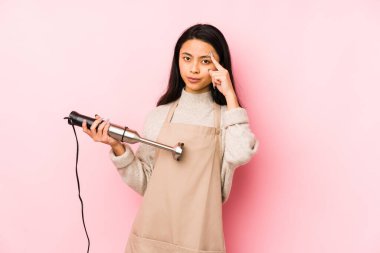 Bir mikseri tutan genç Çinli kadın işaret parmağıyla hayal kırıklığı işareti yapıyor..