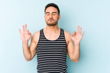 Mavi arka planda izole edilmiş genç beyaz adam yorucu bir günün ardından rahatlıyor. Yoga yapıyor..