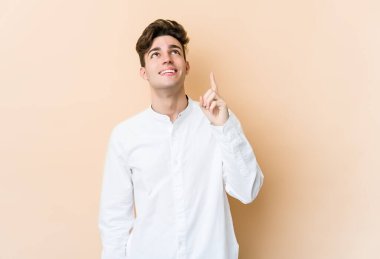 Beyazlı genç bir adam bej arka planda izole edilmiş iki parmağı da boş bir alan gösteriyor..