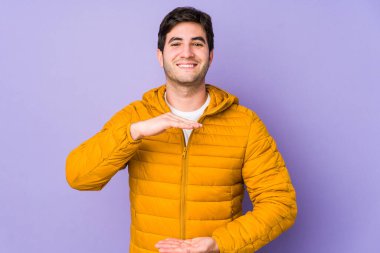 Mor arka planda izole genç bir adam iki eliyle bir şey tutuyor, ürün sunumu..