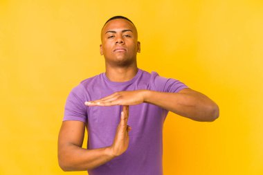 Sarı arka planda izole edilmiş genç latin adam bir mola hareketi gösteriyor..