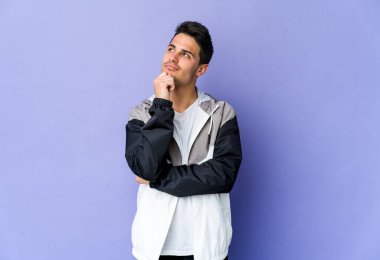 Mor arka planda izole edilmiş genç beyaz adam şüpheli ve şüpheci bir ifadeyle yana bakıyor..