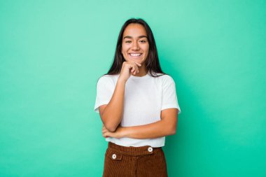 Genç, melez Hintli bir kadın izole edilmiş mutlu ve kendinden emin gülümseyen, elleriyle çenesine dokunan.