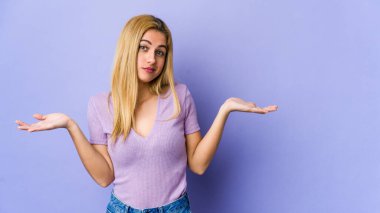 Mor arka planda soyutlanmış genç sarışın bir kadın şüpheli bir tavırla omuz silkiyor..