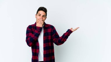 Beyaz arka planda izole edilmiş genç beyaz adam, avuç içi fotokopi alanını elinde tutmaktan etkilenmiş..