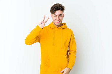 Beyaz arka planda izole edilmiş genç beyaz bir adam neşeli ve kaygısız parmakları olan bir barış sembolü gösteriyor..