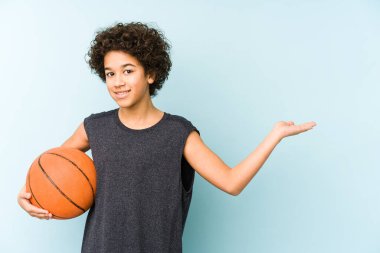 Basketbol oynayan çocuk mavi arka planda izole edilmiş bir şekilde bir avuç içinde fotokopi alanı ve belinde başka bir el tutarken görülüyor..