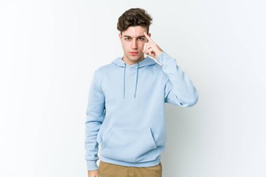 Beyaz arka planda izole edilmiş genç beyaz bir adam şakağı parmağıyla işaret ediyor, düşünüyor ve bir göreve odaklanıyor..