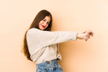 Beyazlı genç bir kadın bej arka planda izole edilmiş, kollarını uzatmış, rahat bir konumda..