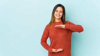 Mavi arka planda izole edilmiş genç bir kadın iki eliyle bir şey tutuyor, ürün sunumu.