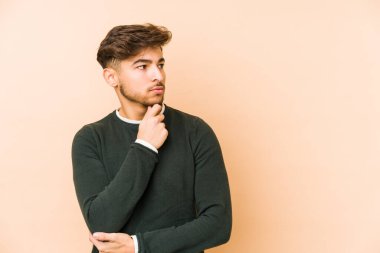 Bej bir arka planda izole edilmiş genç bir Arap şüpheli ve şüpheci bir ifadeyle yana bakıyor..