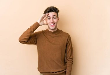 Beyaz tenli genç adam bej arka planda izole edilmiş yüksek sesle bağırıyor, gözleri açık ve elleri gergin tutuyor..