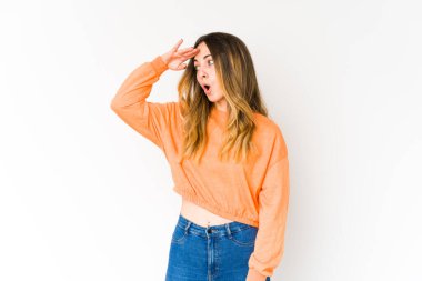 Beyaz arka planda soyutlanmış genç beyaz bir kadın çok uzaklara bakıyor ve elini alnına koyuyor..