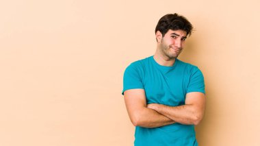 Bej arka planda izole edilmiş genç adam kameraya alaycı bir ifadeyle bakıyor..