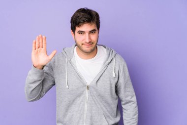 Mor arka planda izole edilmiş genç adam gülümseyerek beş numarayı parmaklarıyla gösteriyor..