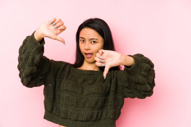 Pembe arka planda izole edilmiş genç Çinli kadın baş parmağını aşağı gösteriyor ve hoşlanmadığını ifade ediyor..
