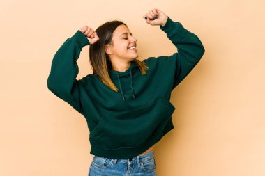 Bej arka planda izole edilmiş genç bir kadın özel bir günü kutluyor, atlıyor ve enerji ile kollarını kaldırıyor..