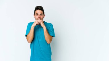 Beyaz arka planda izole edilmiş genç beyaz bir adam şans için dua ediyor, şaşırmış ve ağzını açıp önüne bakıyor..