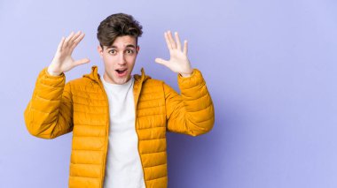 Mor arka planda izole olmuş genç beyaz bir adam zaferi ya da başarıyı kutluyor, şaşırıyor ve şok oluyor..