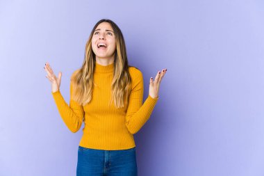 Mor arka planda izole edilmiş genç beyaz kadın gökyüzüne haykırıyor, yukarı bakıyor, hayal kırıklığına uğramış..