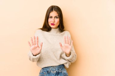 Beyazlı genç bir kadın, bej arka planda izole edilmiş. İğrenme belirtisi gösteren birini reddediyor..