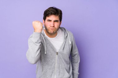 Mor arka planda izole edilmiş genç bir adam kameraya yumruk, agresif yüz ifadesi gösteriyor..