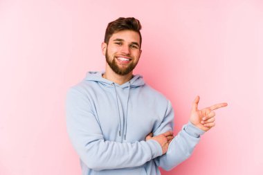 Pembe arka planda izole edilmiş genç beyaz adam işaret parmağıyla işaret ederek gülümsüyor..