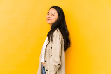 Sarı arka planda izole edilmiş genç Çinli kadın gülümseyen, neşeli ve keyifli bir tarafa bakıyor..